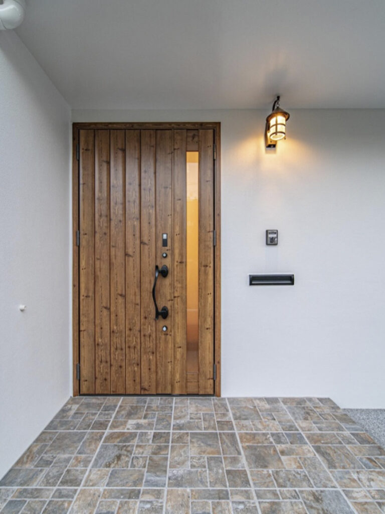 木の扉と灯りに調和する、石目調タイルの玄関ポーチ